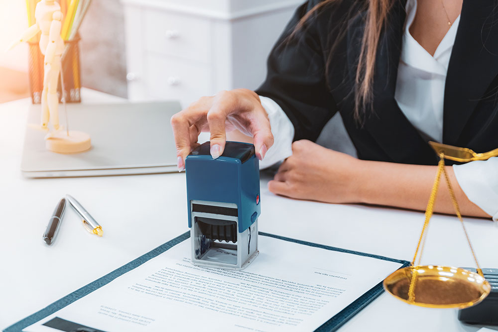 Female notary stamping document agreement at table, close up.