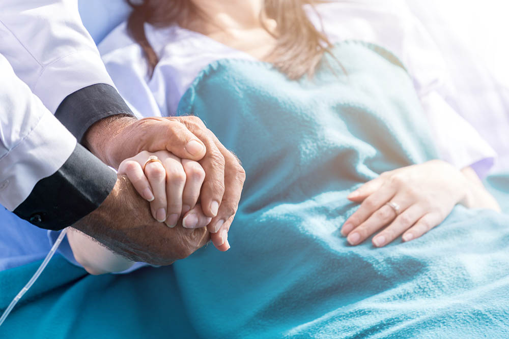 Male doctor holding female patient hand on the hospital bed.