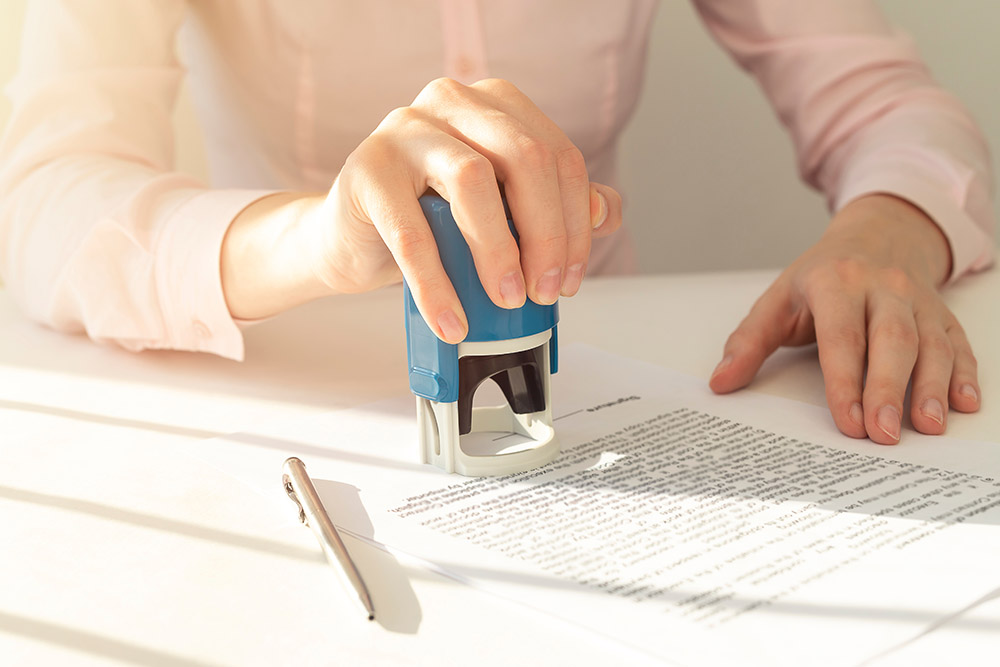 young notary public sitting at the desk in office and stamping document contract