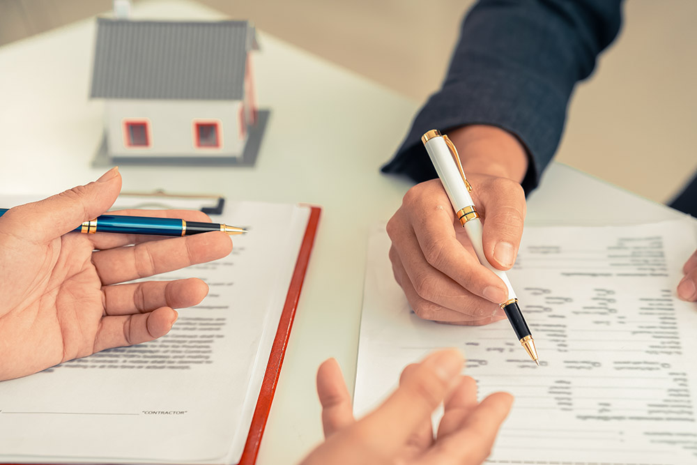 signing a contract next to a model home, symbolizing home owners