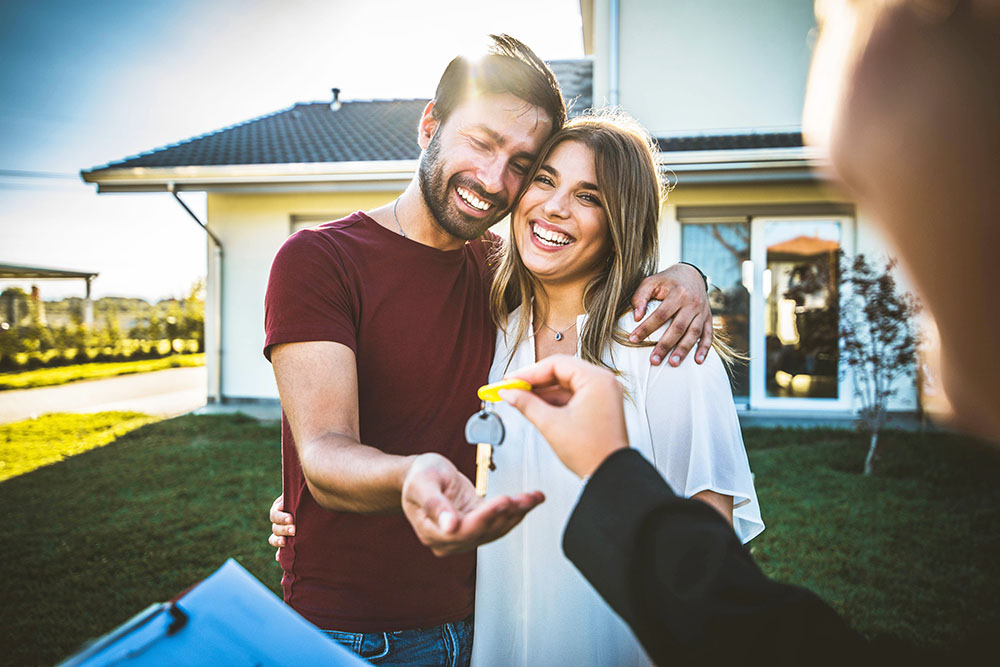 happy millennial couple receiving keys from realtor after buying a home