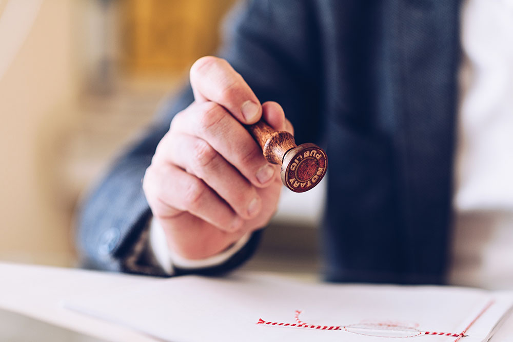 close up of a notary's hand stamping with approved stamp on certificate or document public.