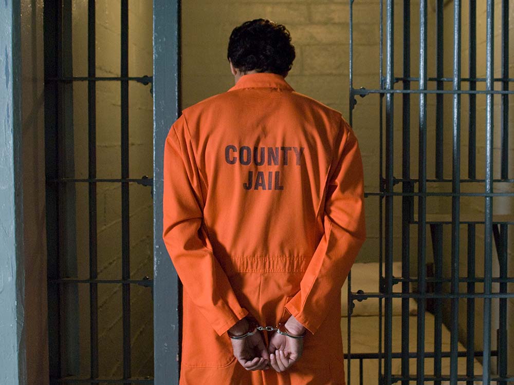 man wearing orange jail clothes next to cell